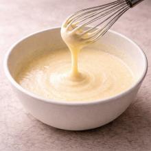 Pale creamy egg mixture falling from a whisk in a ribbon